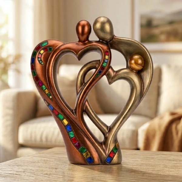 Bronzen beeld van twee figuren die samen twee harten vormen, met gekleurde mozaieksteentjes, op een tafel in een woonkamer