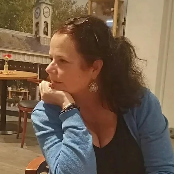 Paula Damen-van Eijk in gedachten, met haar hand onder haar kin, aan een tafel in een cafe